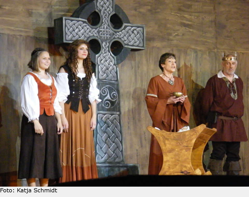 Grace' Amme Evleen (Irmgard Kühnle-Lange) singt die alten irischen Segnungen, ihre Freundin Majella (Franziska Brenner) steht an ihrer Seite, ebenso Donals Vater Hugh (Dieter Wolf). Tiernan trägt den kleinen Eoghan zum Taufbecken. the pirate queen 33